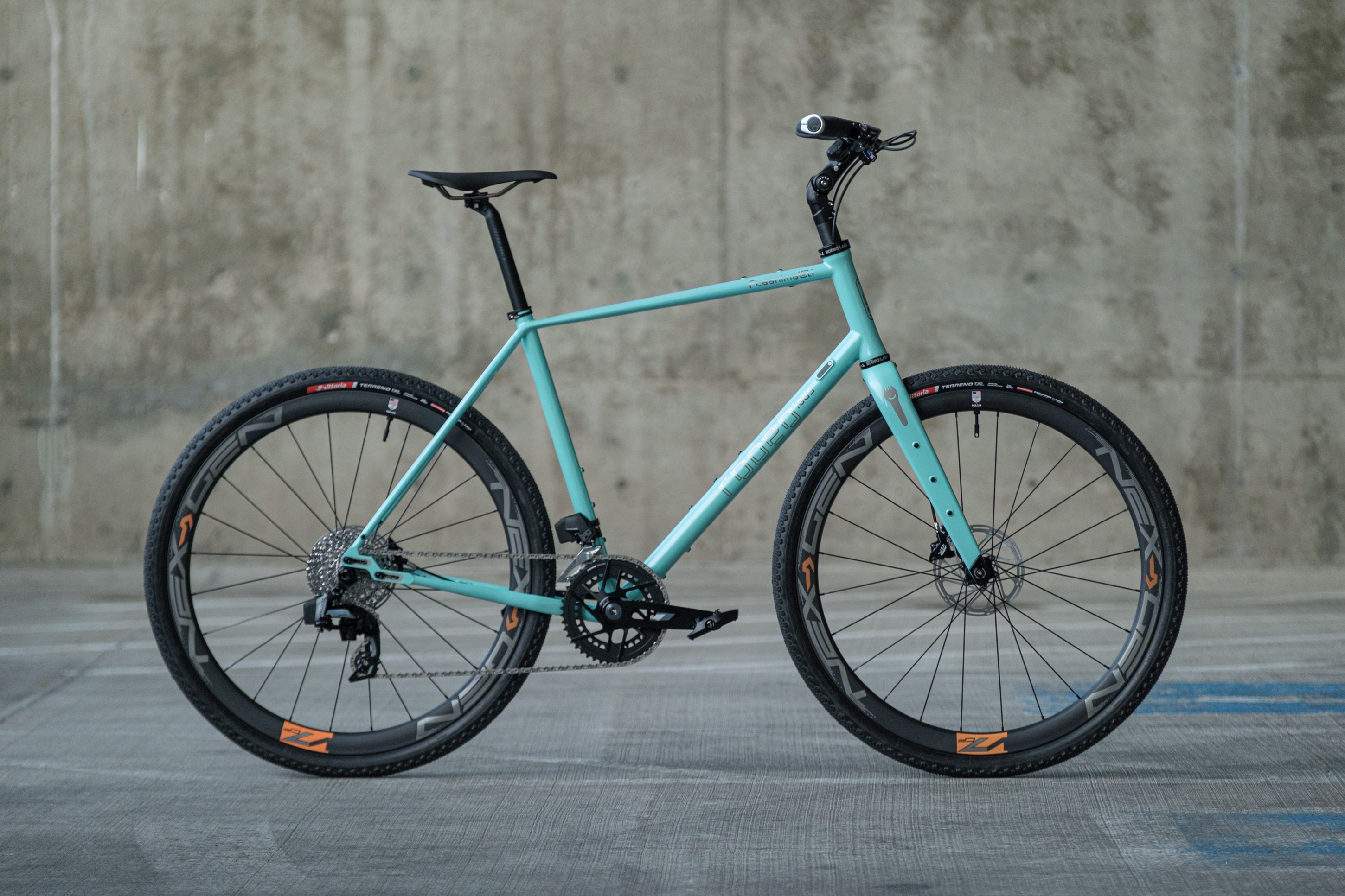 A light blue bicycle with black wheels and tires, positioned against a concrete wall.