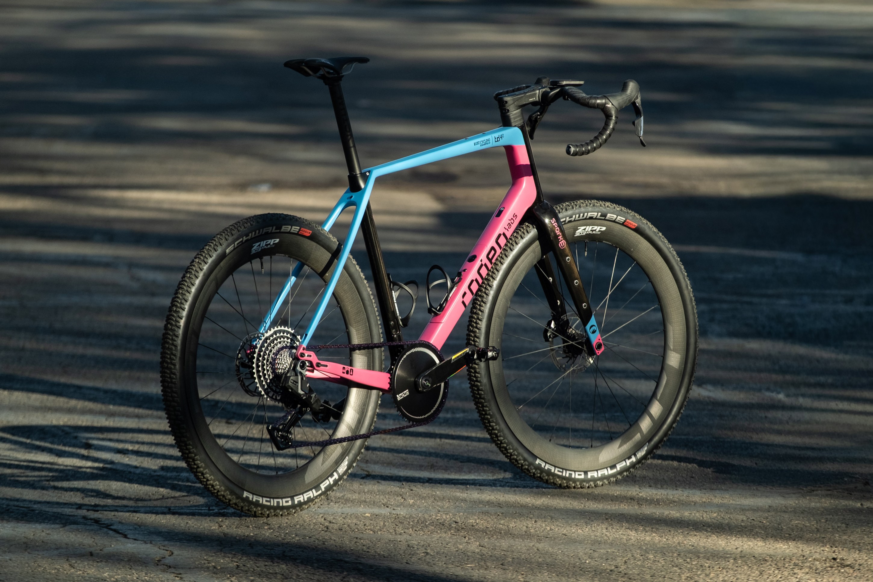 A colorful modern bicycle with a pink and blue frame, featuring wide tires and a sleek design, positioned on a paved surface.