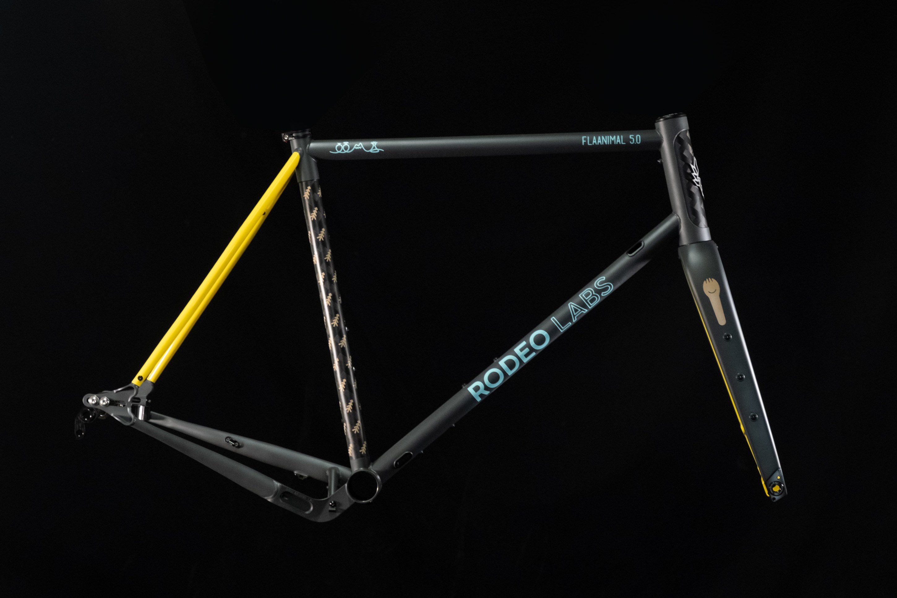 A close-up image of a bicycle frame showcasing a sleek design with a combination of grey, yellow, and black colors. The frame features the 'RODEO LABS' branding and visible mounting points.