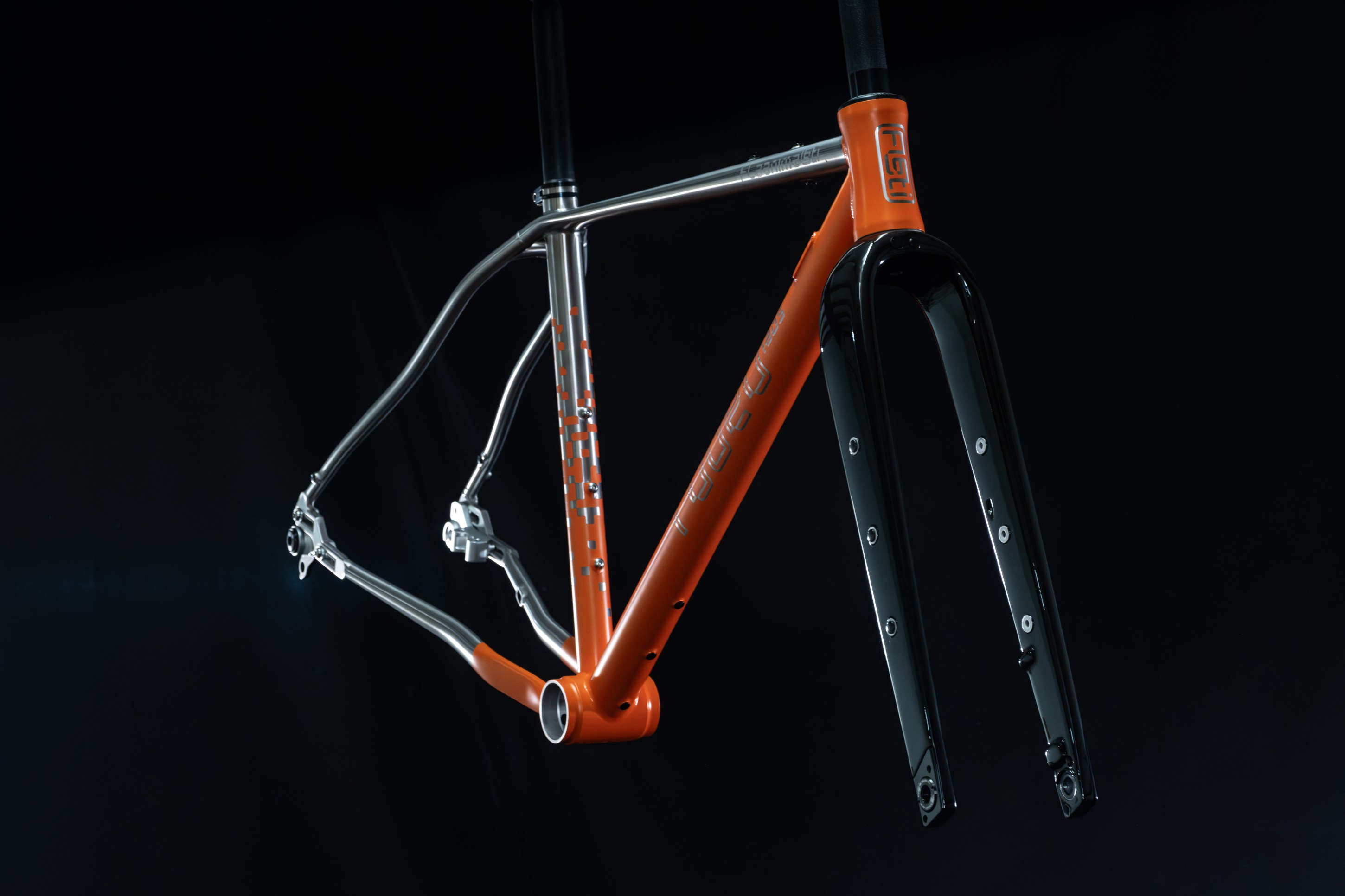A close-up image of an orange and silver bike frame suspended against a black background, featuring a black fork and detailed construction elements.