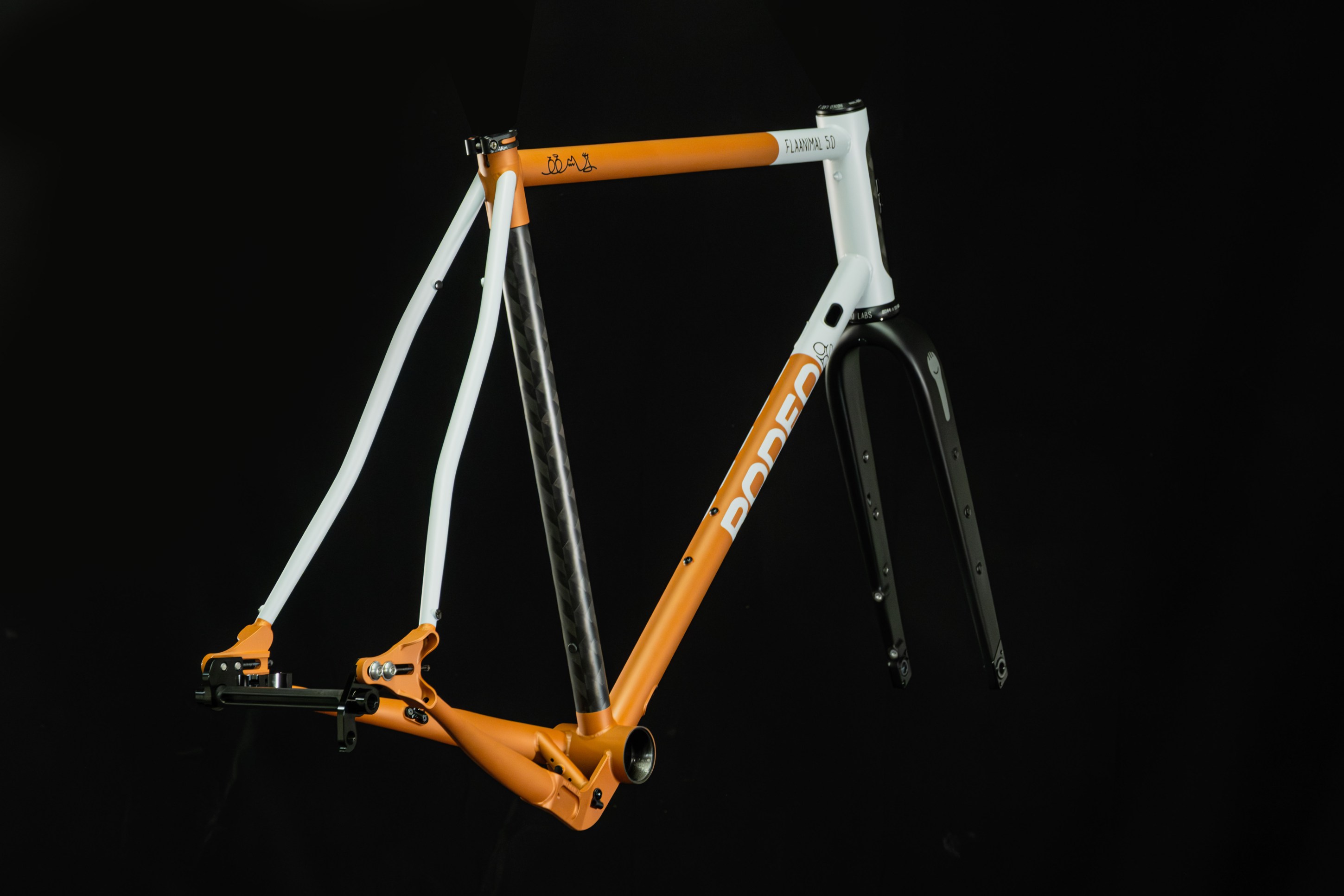 A close-up view of a bicycle frame in orange, white, and black colors, displayed against a black background.