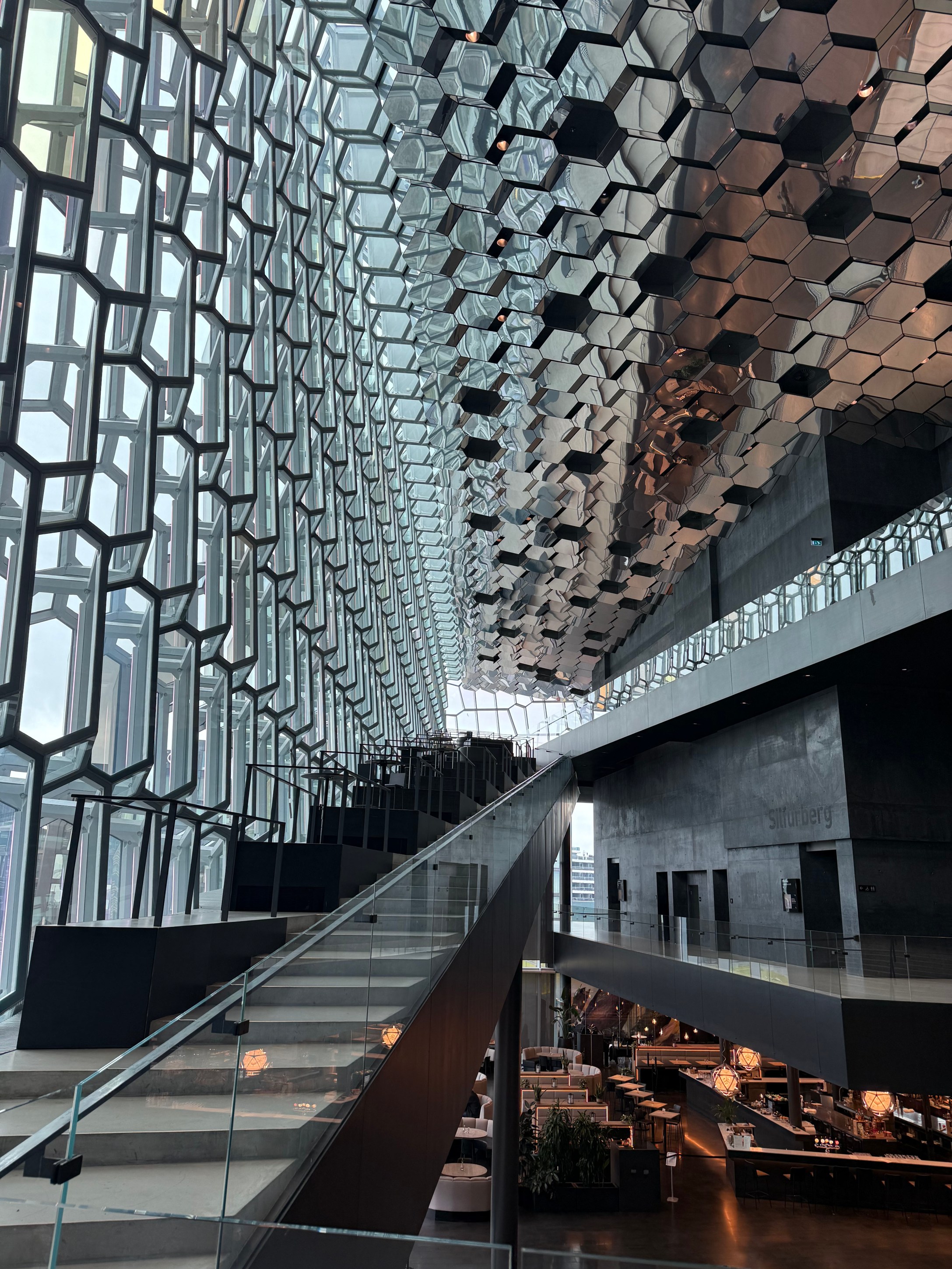 Interior view of a modern architecture space featuring a large hexagonal glass facade, showcasing intricate light reflections and a sleek staircase leading to an upper level.