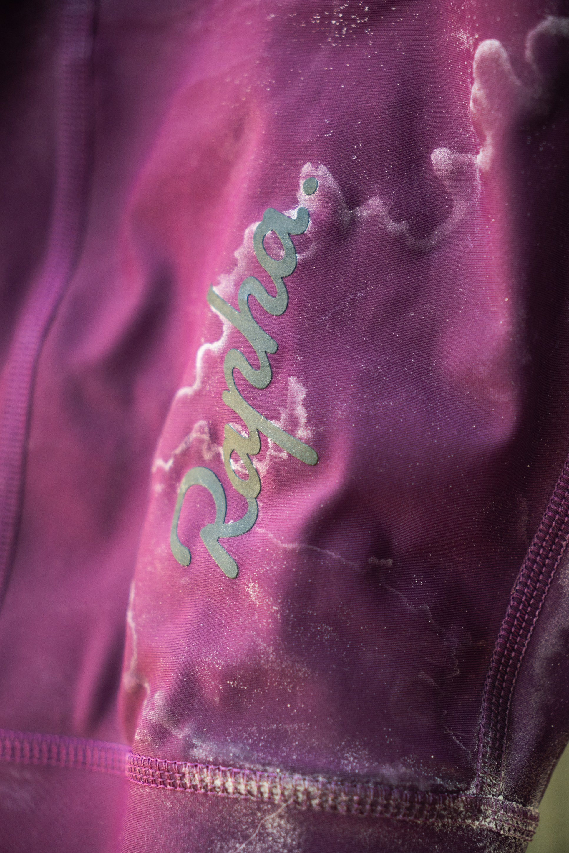 Close-up of a purple cycling jersey featuring the word 'Rapha' in a cursive font.