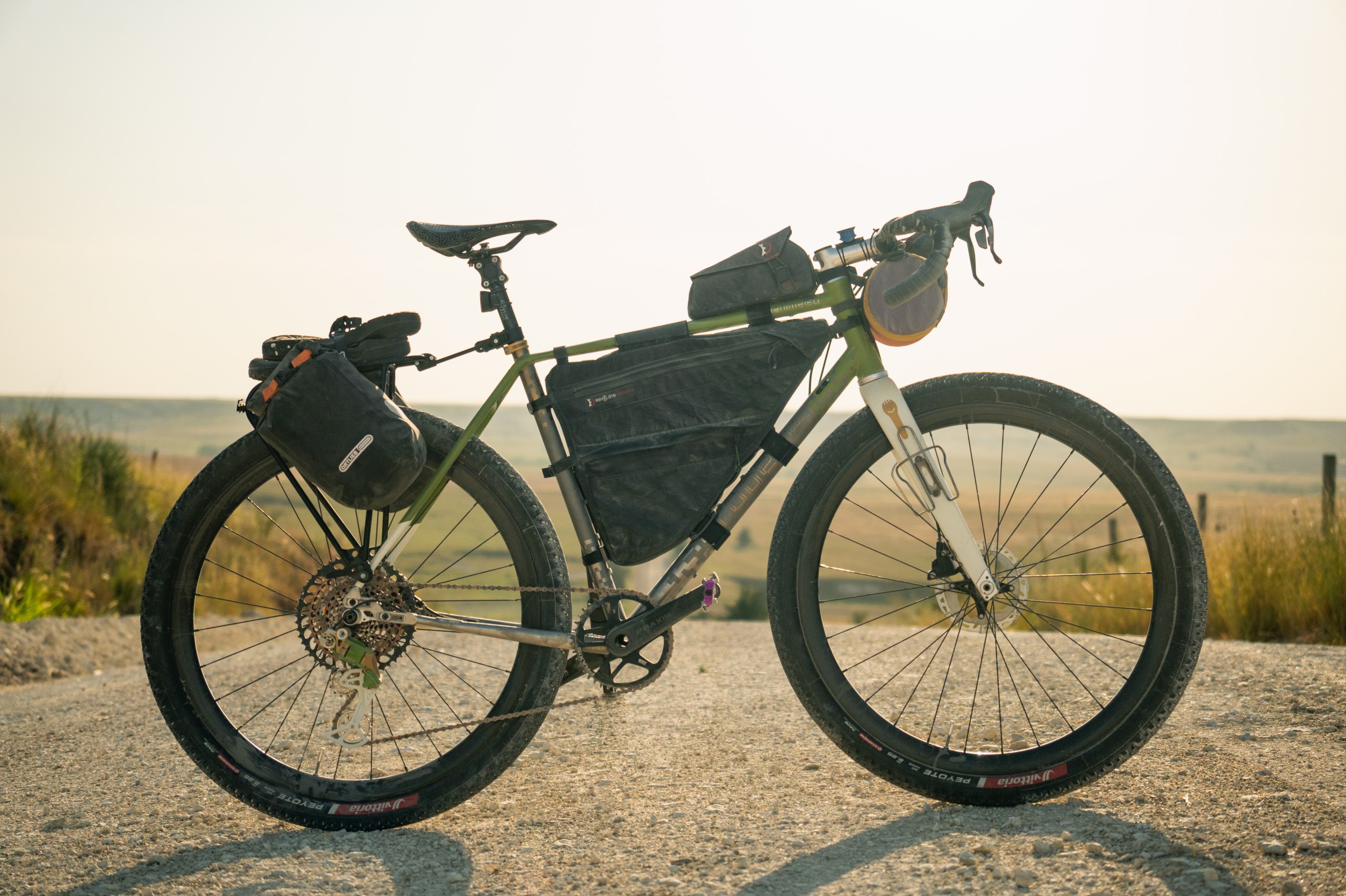 Close-up view of a touring bicycle with bags, parked on a gravel road against a scenic landscape backdrop.