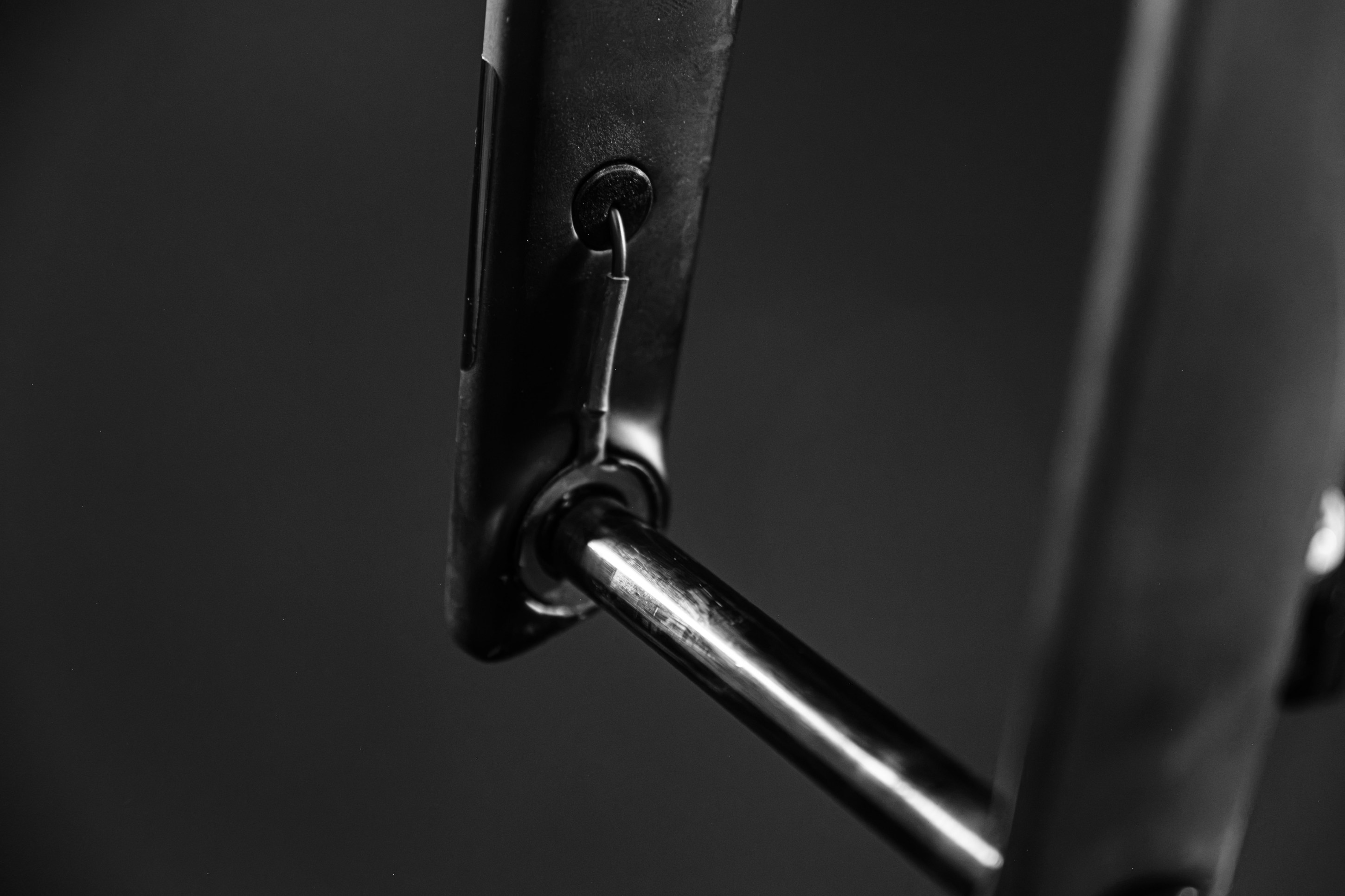 Close-up image of a metallic latch mechanism with a pin and a cylindrical rod against a dark background.
