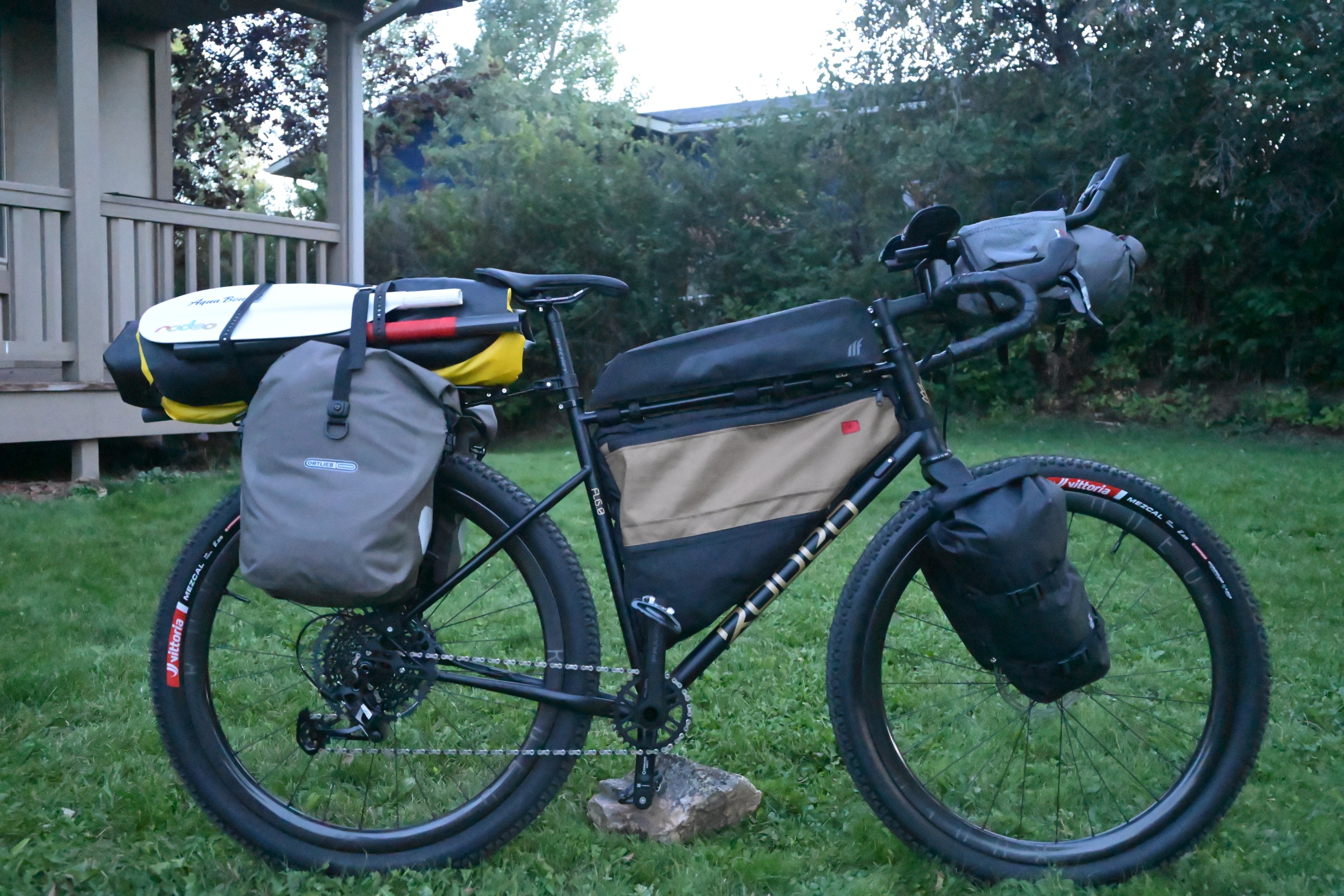A fully equipped bicycle with multiple panniers and bags, parked on grass in a backyard setting.
