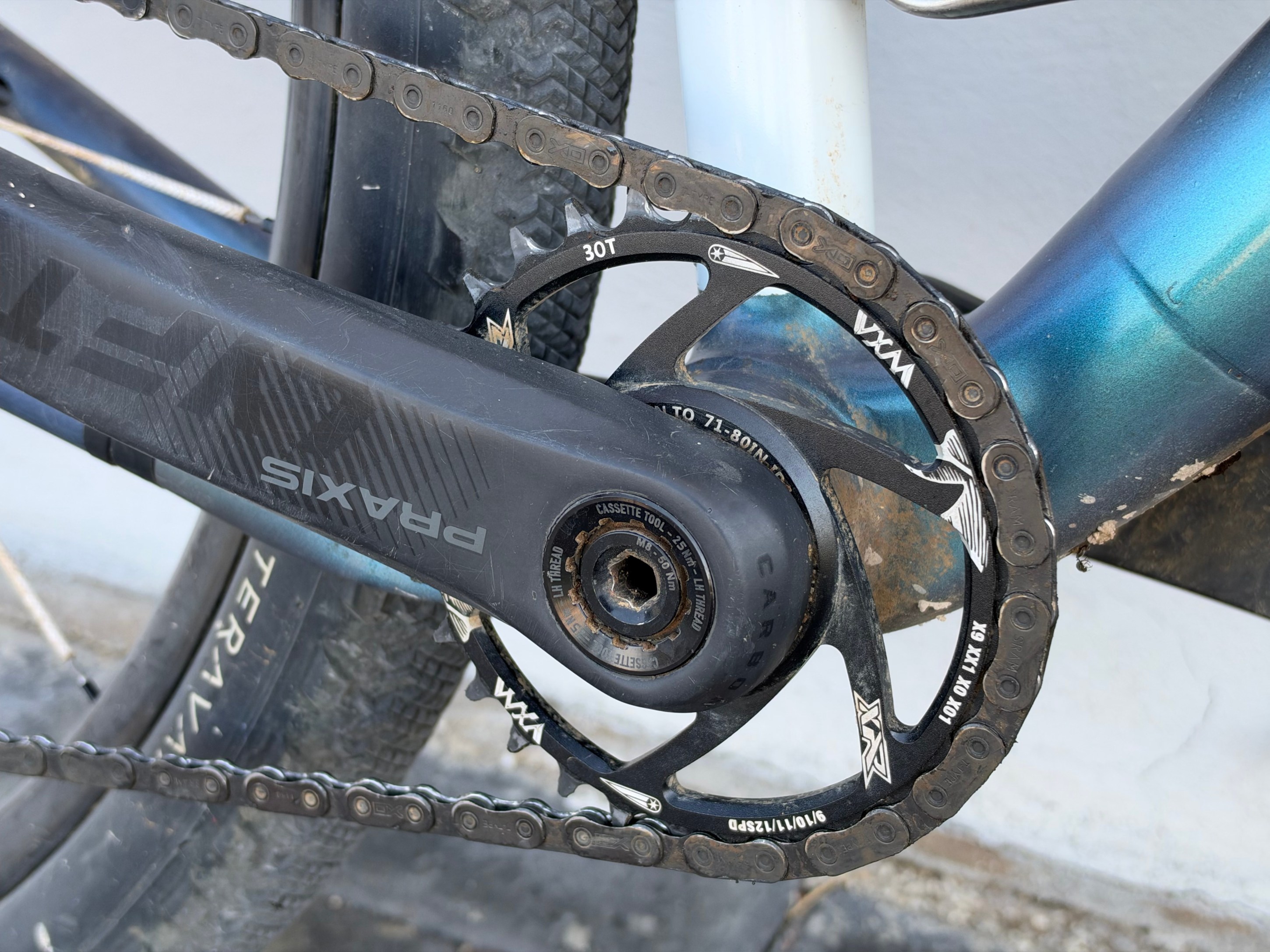 Close-up of a bicycle's crankset with a black chainring, chain, and pedal attached to a carbon frame.