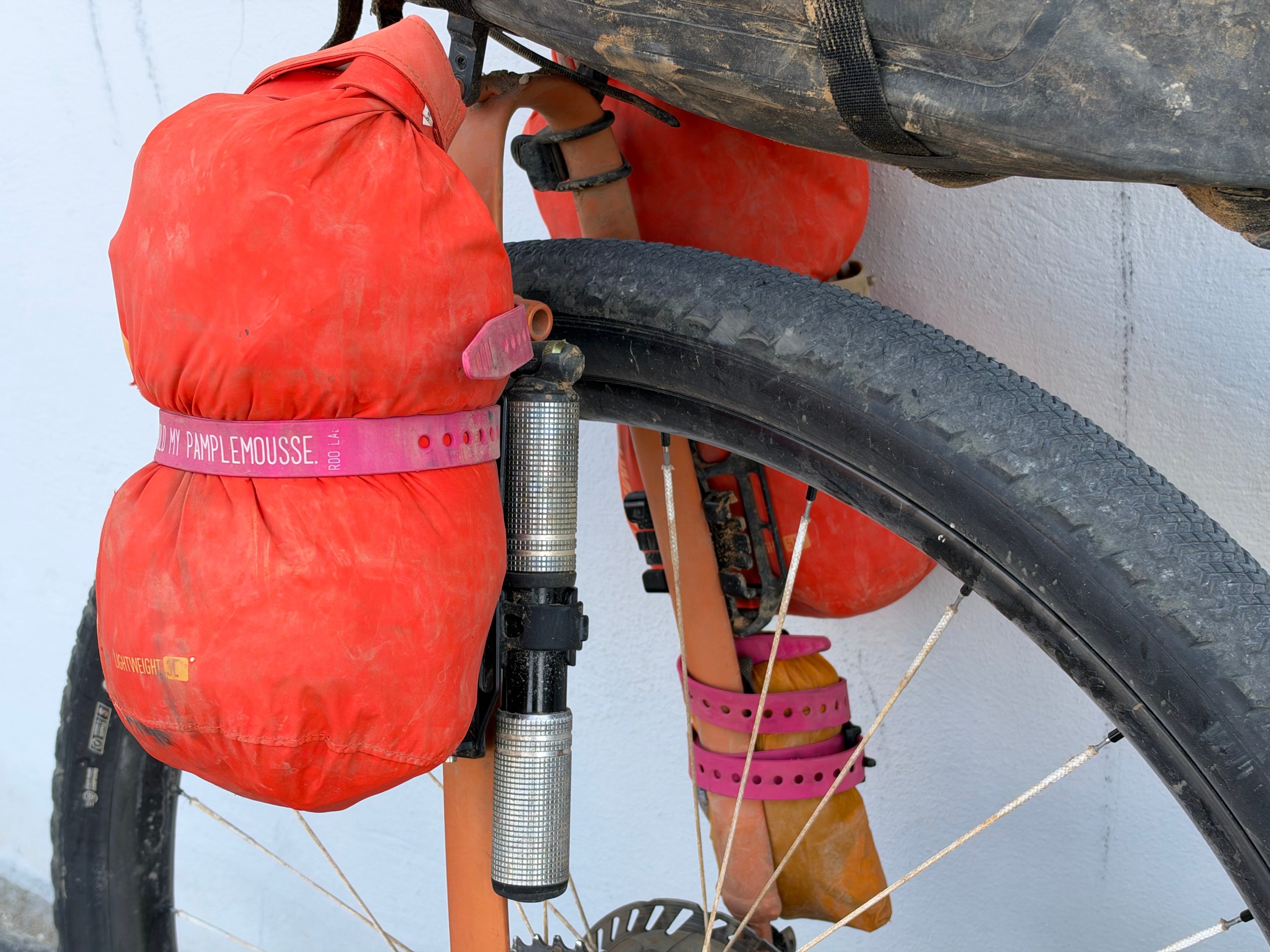 Close-up of a bicycle's front wheel with red waterproof bags secured to the frame, showcasing a lightweight design and pink straps for attachment.