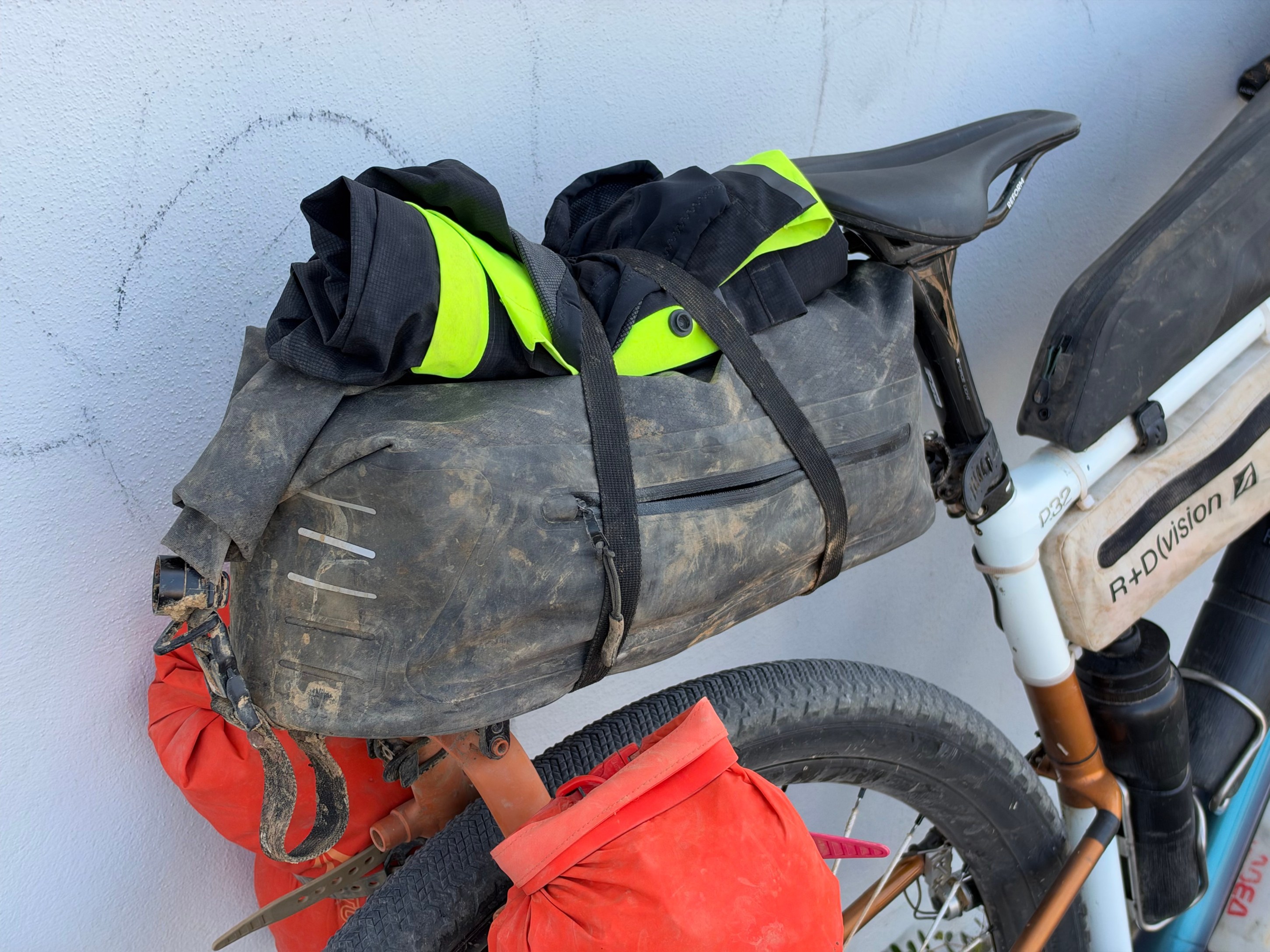 A close-up of a bike's saddle with a dirty bag attached, holding folded black clothing with neon yellow stripes.