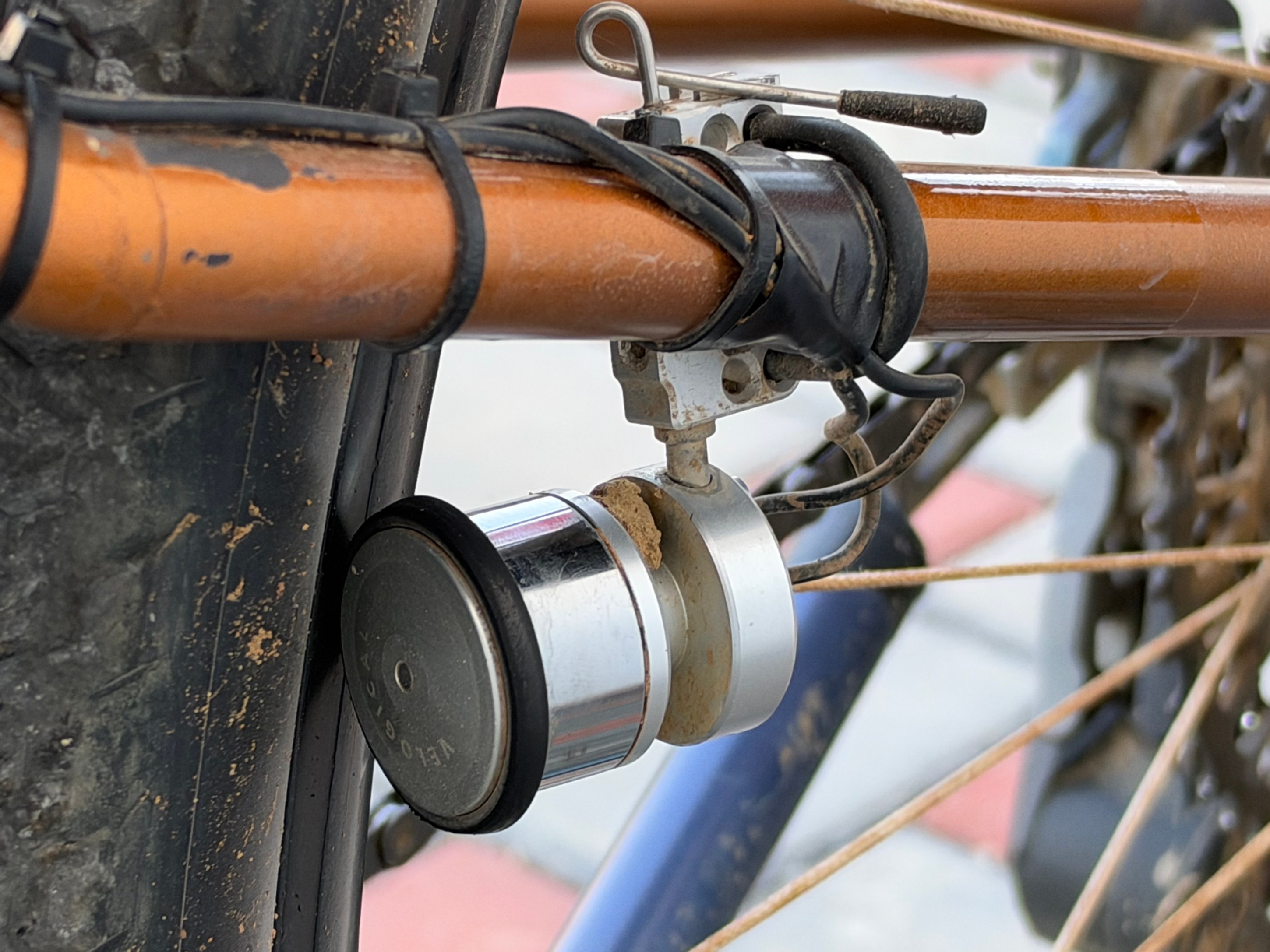 Close-up of a bicycle's rear hub with a silver and black bicycle bell mounted on the frame, showing dirt and wear.