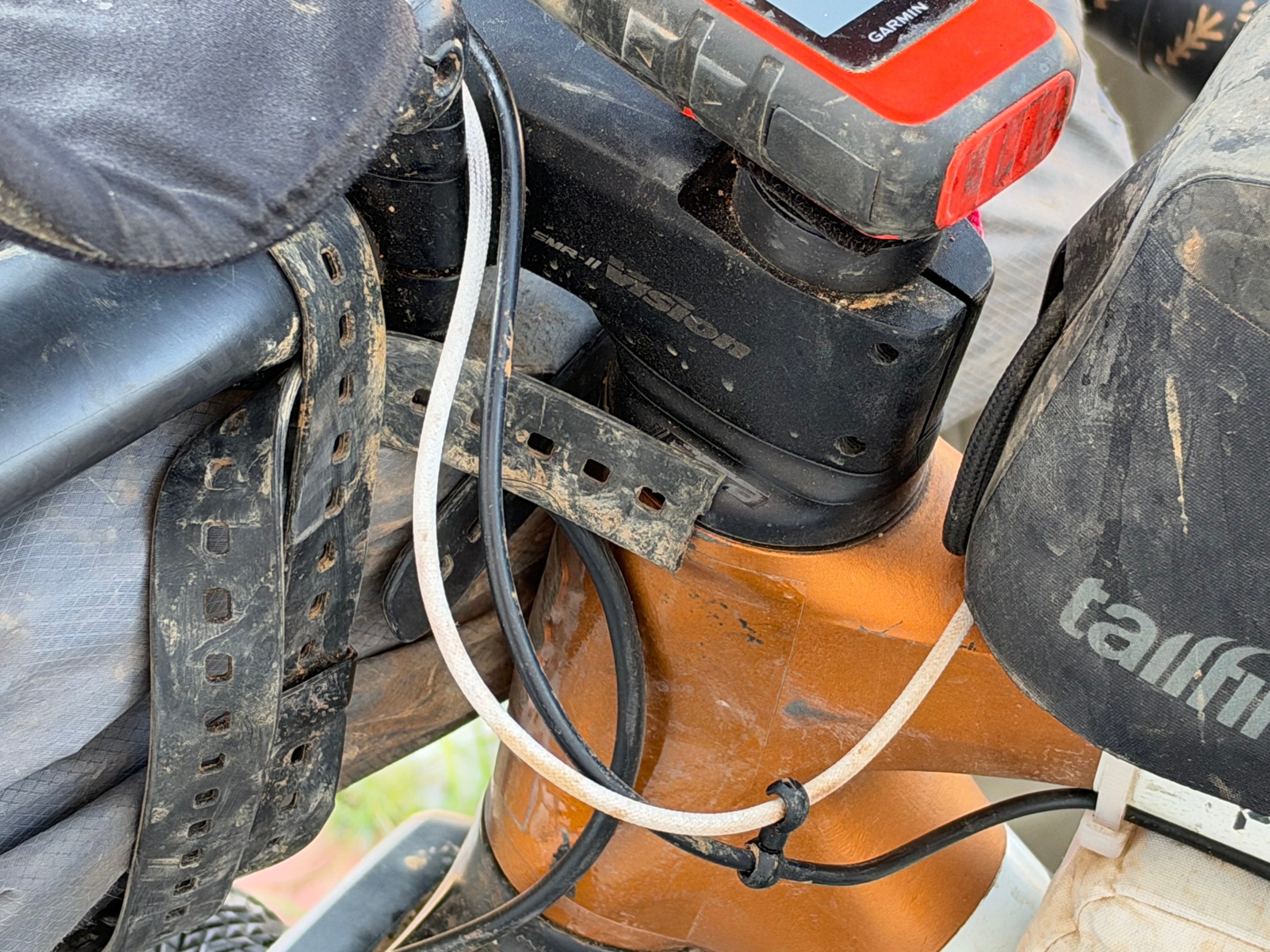 Close-up view of a bicycle's handlebar area showing several cables, a GPS device, and a seat with a protective cover.