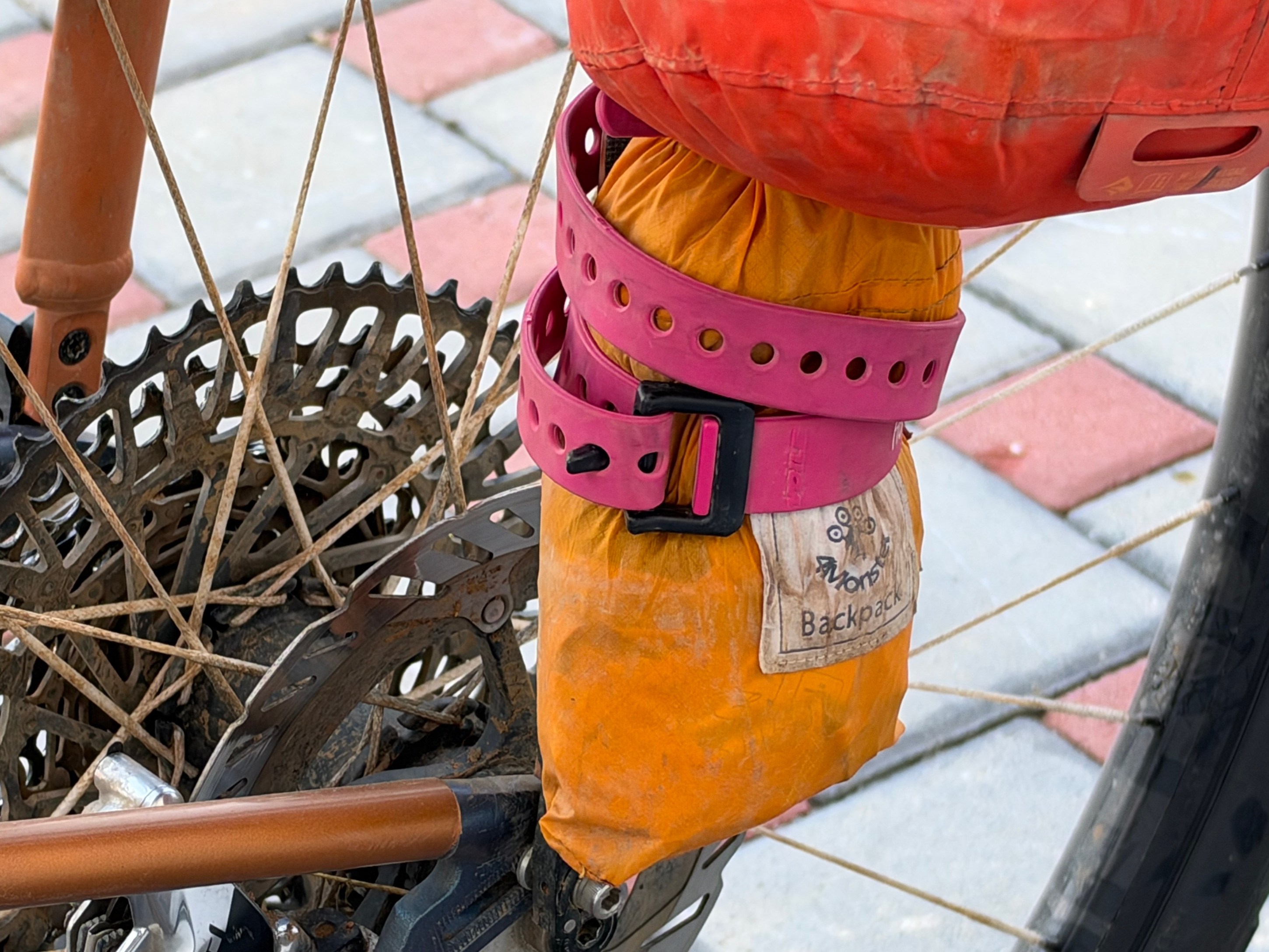 Close-up of a bicycle's rear wheel with a colorful bag secured by a pink strap, resting against the frame.